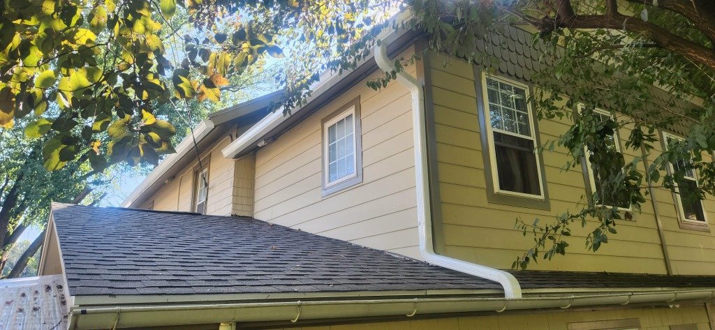 Tan siding home with new white gutters fall